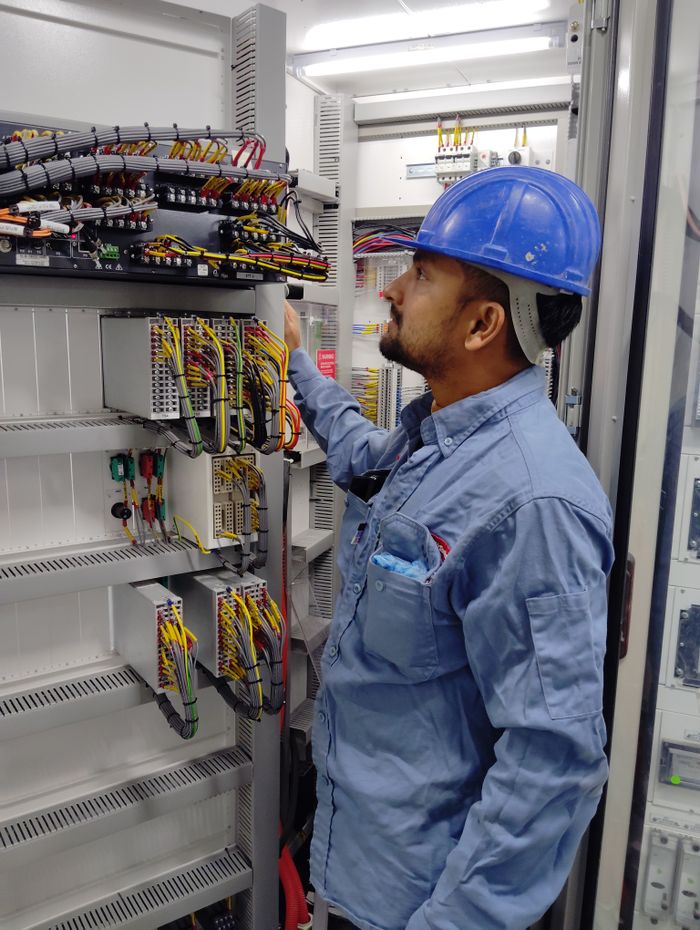 Services Electrician in blue helmet checking control panel wiring for safety compliance.