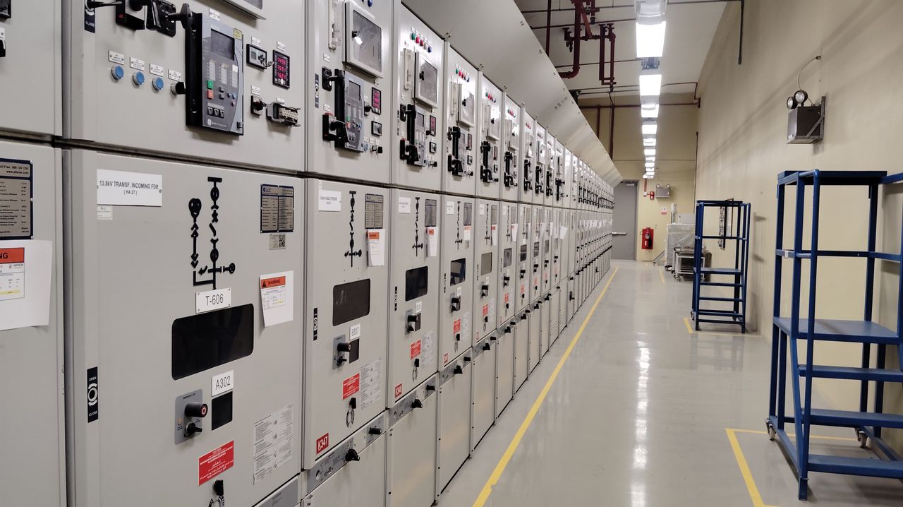 Services Long row of control panels in an industrial electrical control room, well-lit and spacious.